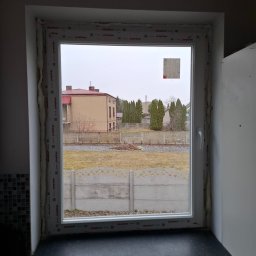 SKO-MONT OKNA - Montaż okna PCV w Bystrzanowicach. Widok na zewnątrz przez świeżo osadzone okno z pianką montażową. Nowa stolarka okienna z widokiem na ogród i dom.