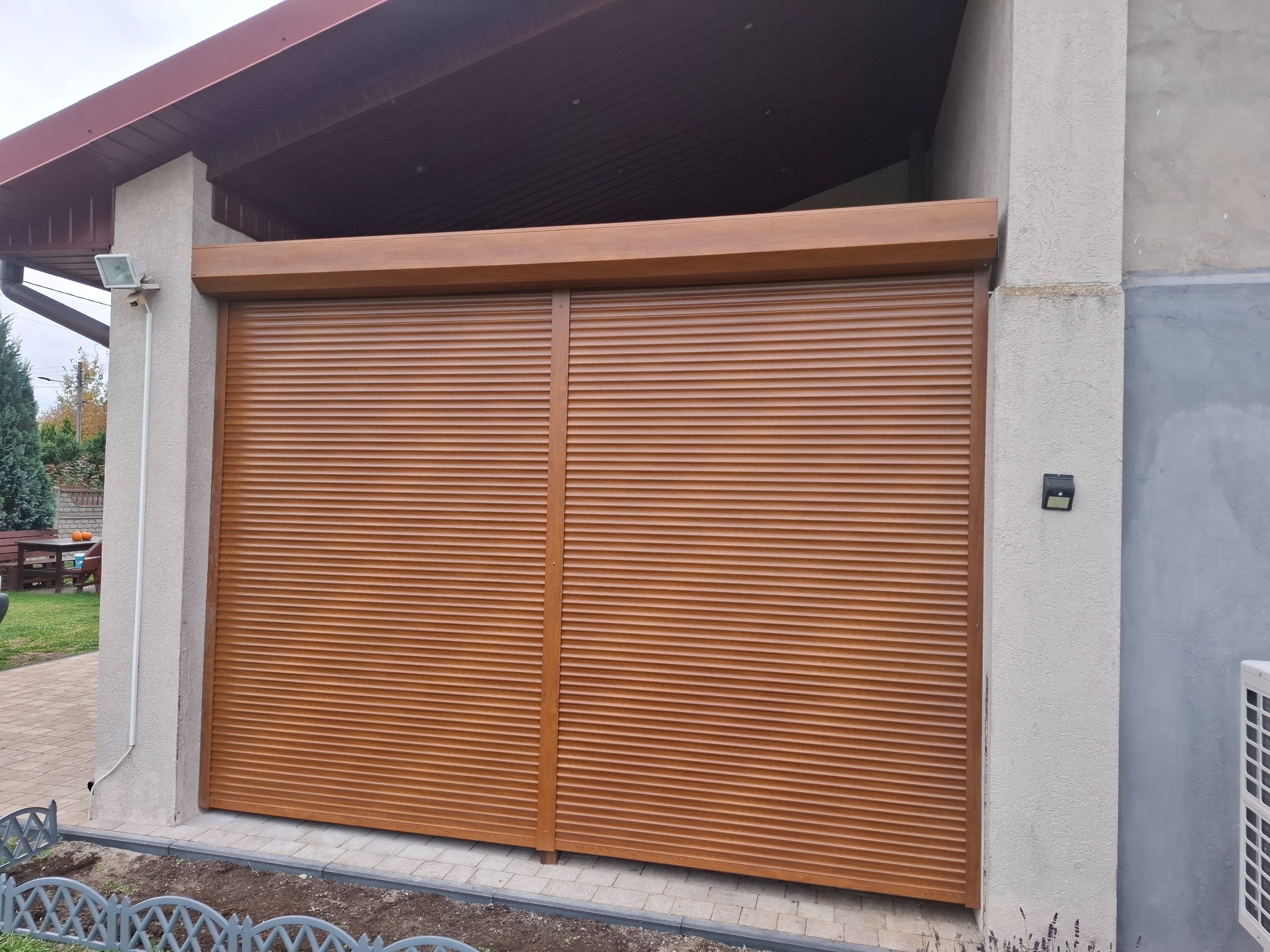 Brązowe rolety zewnętrzne, zamknięte, zamontowane na wjeździe do garażu. Widoczna faktura rolet i elementy konstrukcyjne w zbliżonym odcieniu brązu.