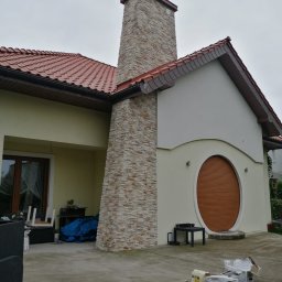 Zakład Remontowo-Budowlany Czesław Kamiński - Elewacja domu jednorodzinnego z kominem wykończonym kamieniem dekoracyjnym, widoczne puszki i kartony po materiałach budowlanych na tarasie.