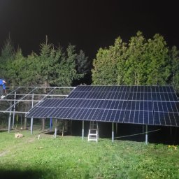 WEAVER STORK SPÓŁKA Z OGRANICZONĄ ODPOWIEDZIALNOŚCIĄ - Montaż paneli fotowoltaicznych na metalowej konstrukcji w ogrodzie, widoczni dwaj pracownicy, jeden na rusztowaniu, drugi na trawniku, nocna sceneria.