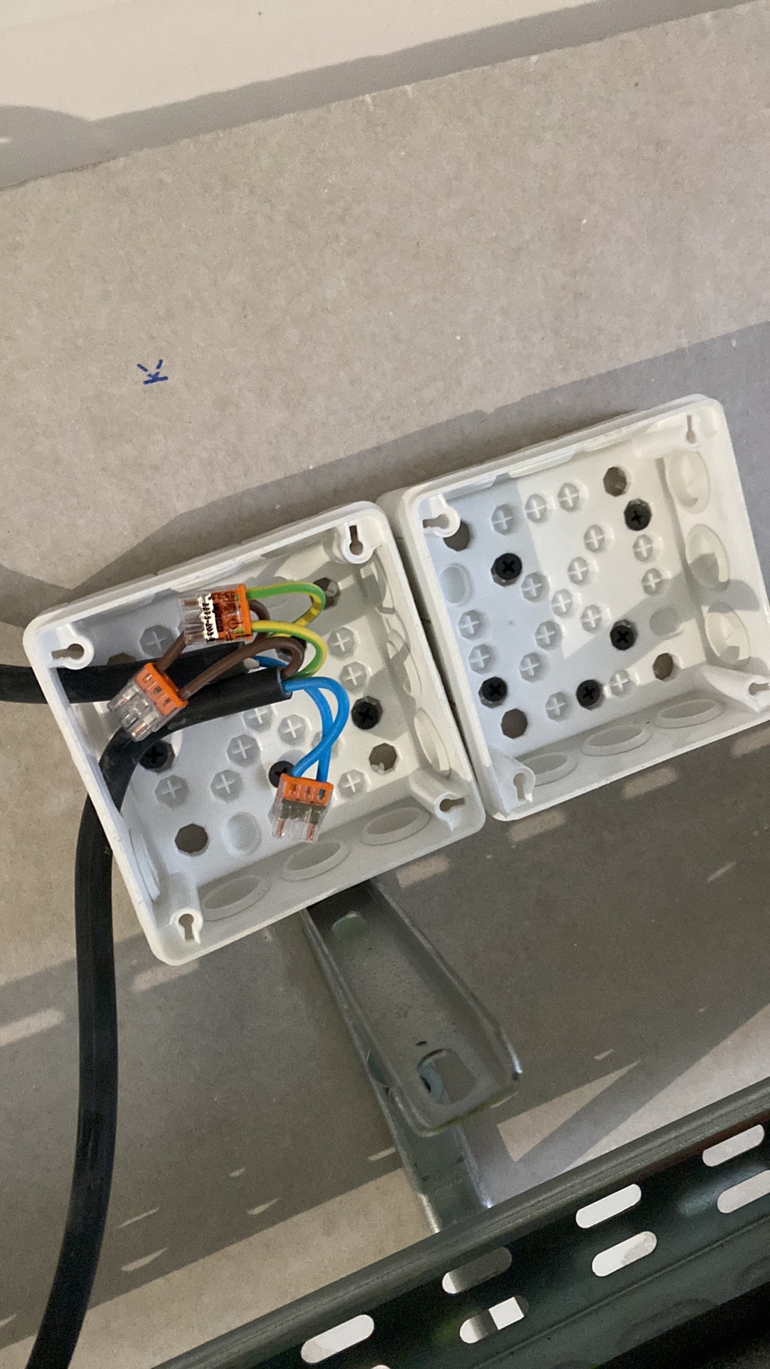 Otwarta puszka elektryczna z przewodami połączonymi złączkami WAGO, widoczne kable w kolorach: czarnym, brązowym, zielono-żółtym i niebieskim, obok druga puszka z czarnymi śrubkami, całość...