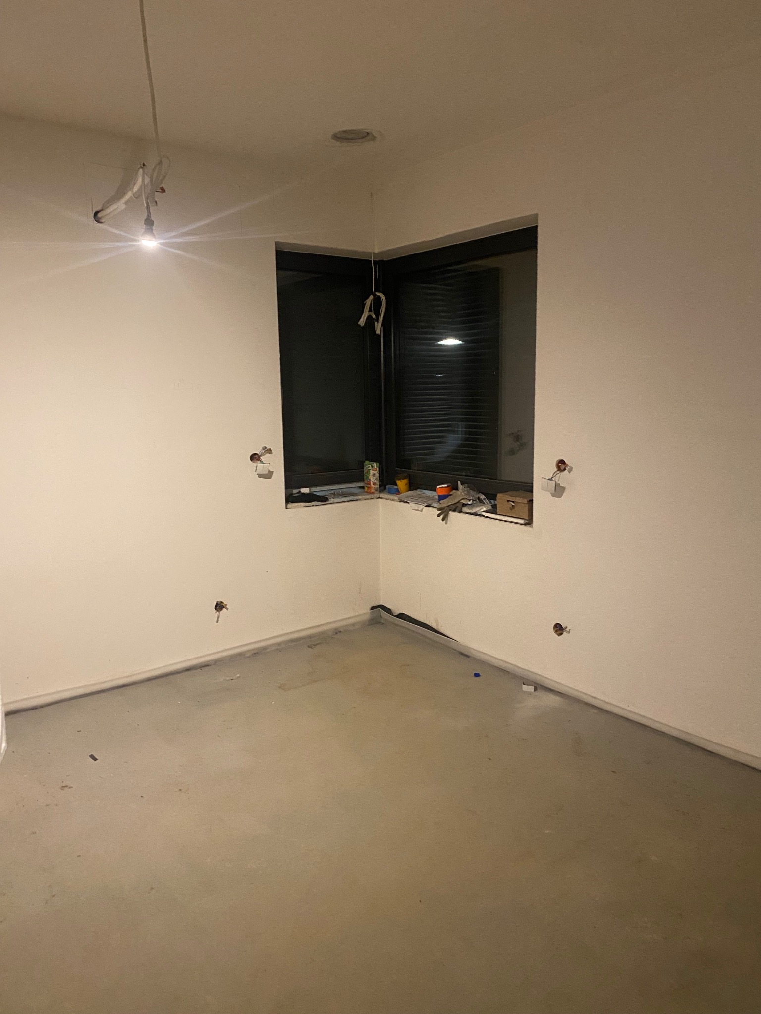 Pokój w trakcie remontu, widoczne przygotowane punkty elektryczne na ścianach, przewody wystające z sufitu i narzędzia na parapecie okna.