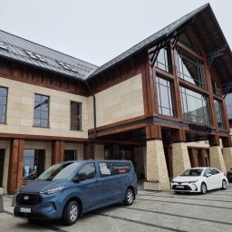 KLIMATYZATORY POLSKA - Niebieski samochód dostawczy z reklamą usług klimatyzacyjnych firmy z Lubartowa zaparkowany przed budynkiem z drewnianą konstrukcją i napisem 'TARNOW'.