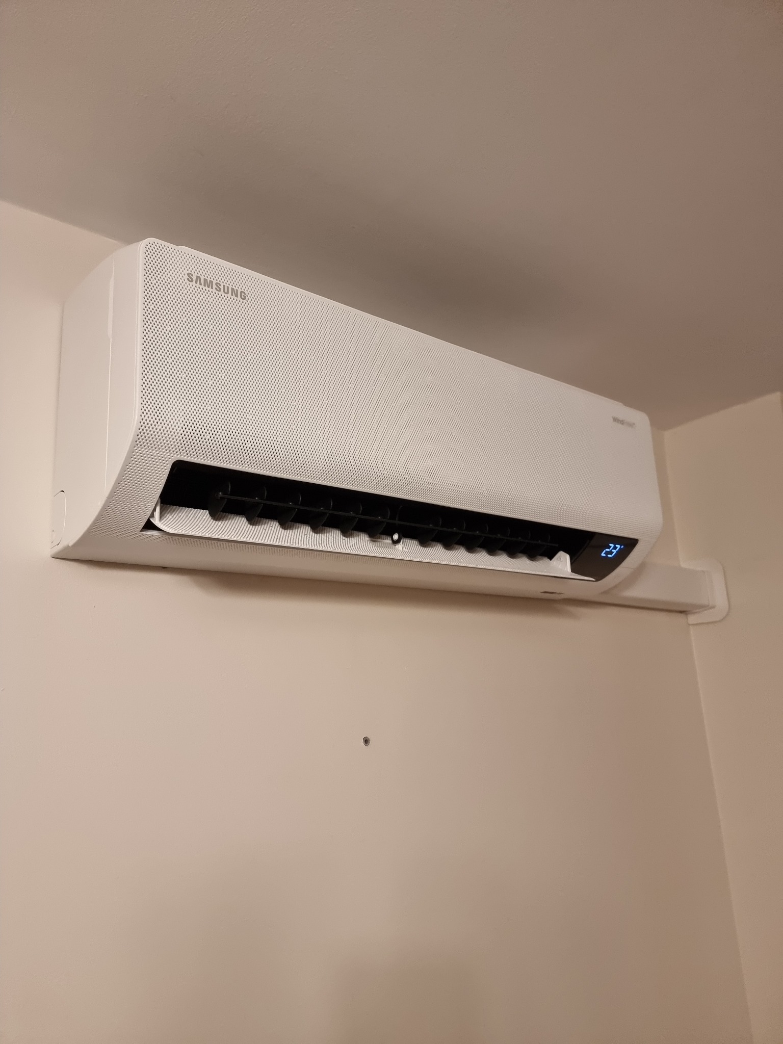 Biała klimatyzacja Samsung zamontowana na jasnej ścianie, widoczny wyświetlacz wskazujący temperaturę 23 stopnie.