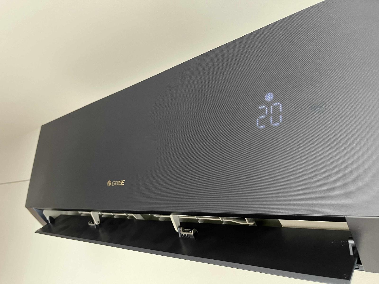 Zamontowany, czarny klimatyzator marki Gree z otwartą klapką, wyświetlający temperaturę 20 stopni Celsjusza i symbol śnieżynki.