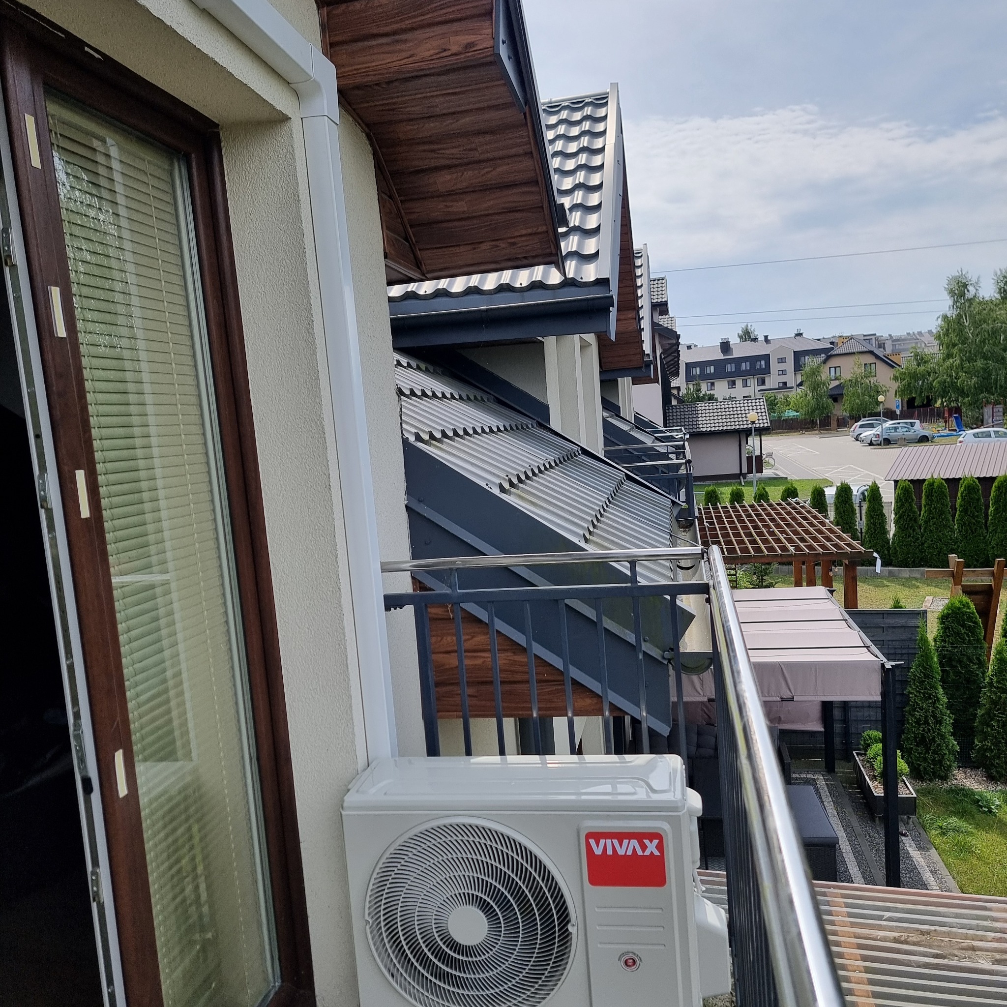 Zewnętrzna jednostka klimatyzacji VIVAX zamontowana na balkonie nowoczesnego apartamentu, widok na osiedle z zielenią.