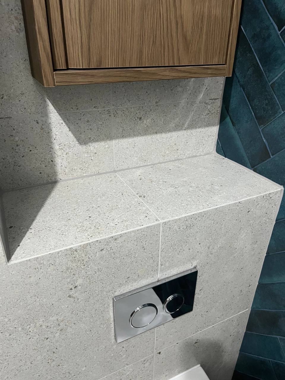 Detale wykończenia łazienki: płytki imitujące kamień, zabudowa WC z drewnianą szafką i przycisk spłukujący. Minimalistyczny design i precyzyjne wykonanie.