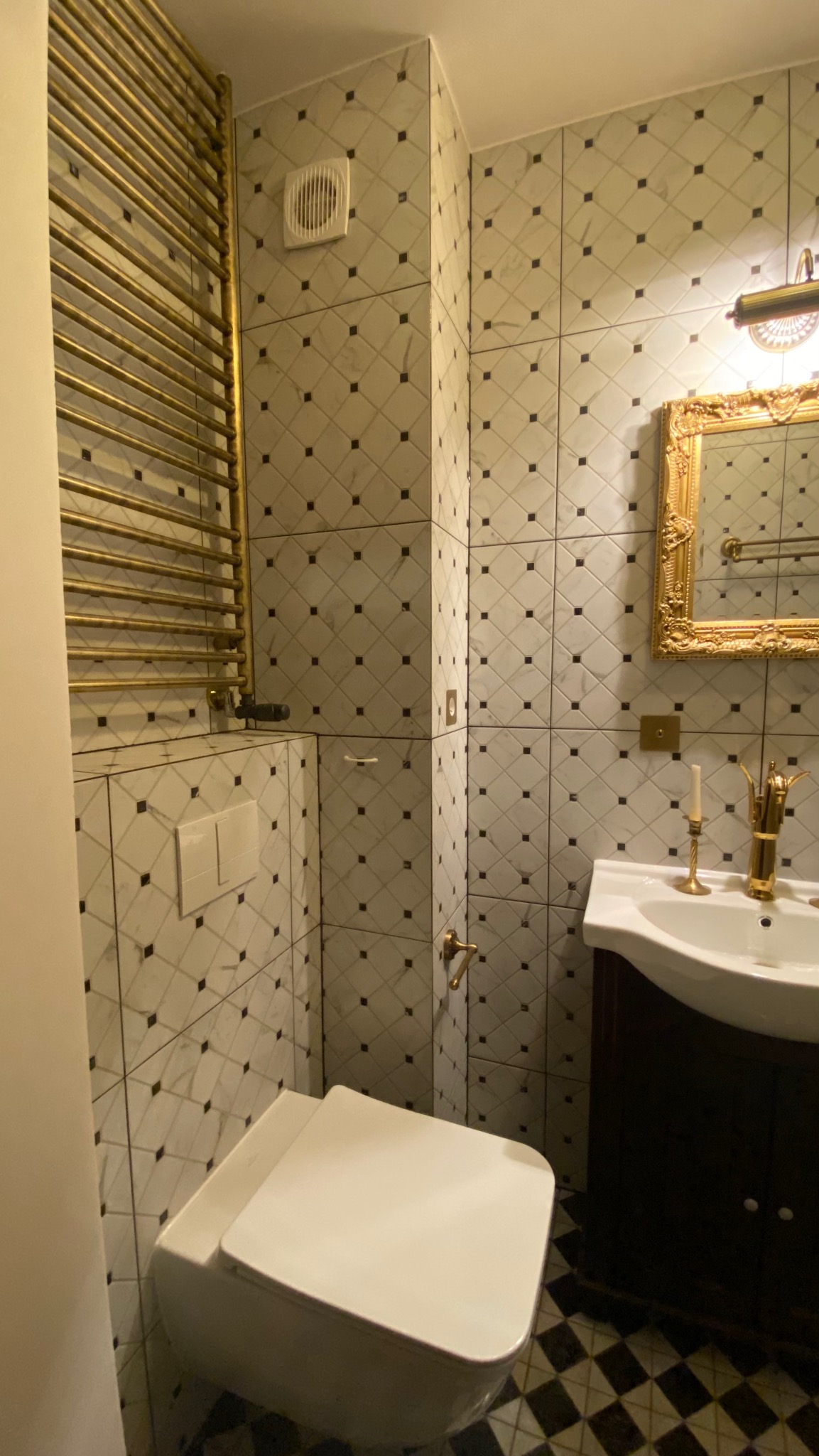 Elegancka łazienka z marmurowymi płytkami w romby, złotym grzejnikiem i lustrem w ozdobnej ramie. Umywalka nablatowa i toaleta w stylu retro.