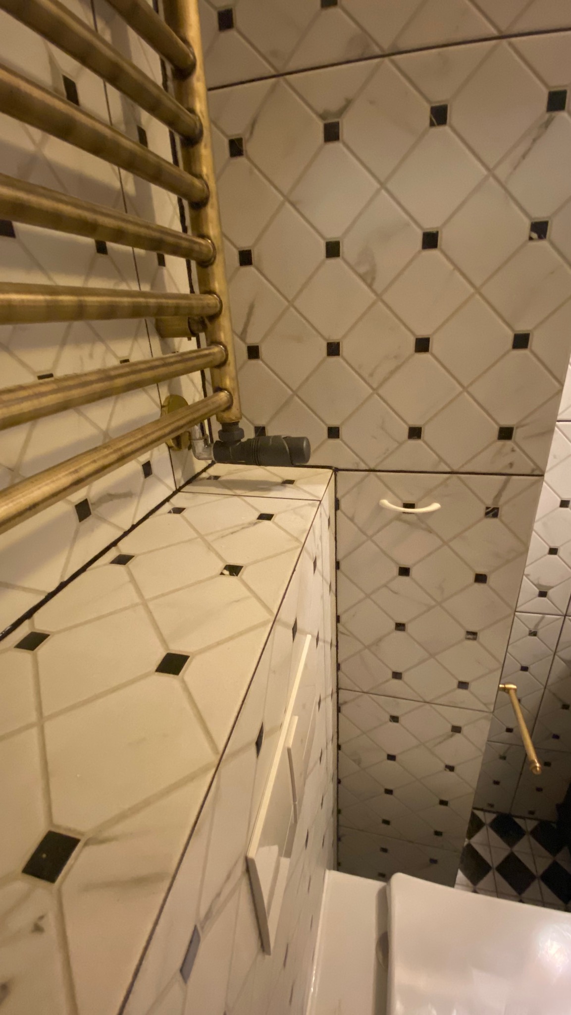 Wykończona łazienka: białe płytki z czarnymi akcentami, złoty grzejnik drabinkowy i biała szafka. Ujęcie z góry, prezentujące detale wykończenia.