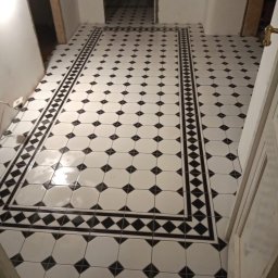 Home & Trade Tomasz Gliński - Ułożona podłoga z białych i czarnych płytek w geometryczny wzór, z wyraźnym obramowaniem w korytarzu, widoczne niedokończone ściany i framugi drzwi.