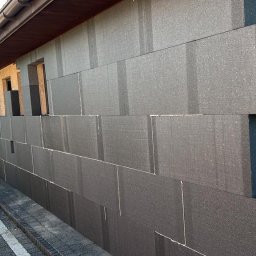 Home & Trade Tomasz Gliński - Ocieplanie ściany domu styropianem grafitowym, widoczna drabina oparta o budynek i tabliczka z adresem.