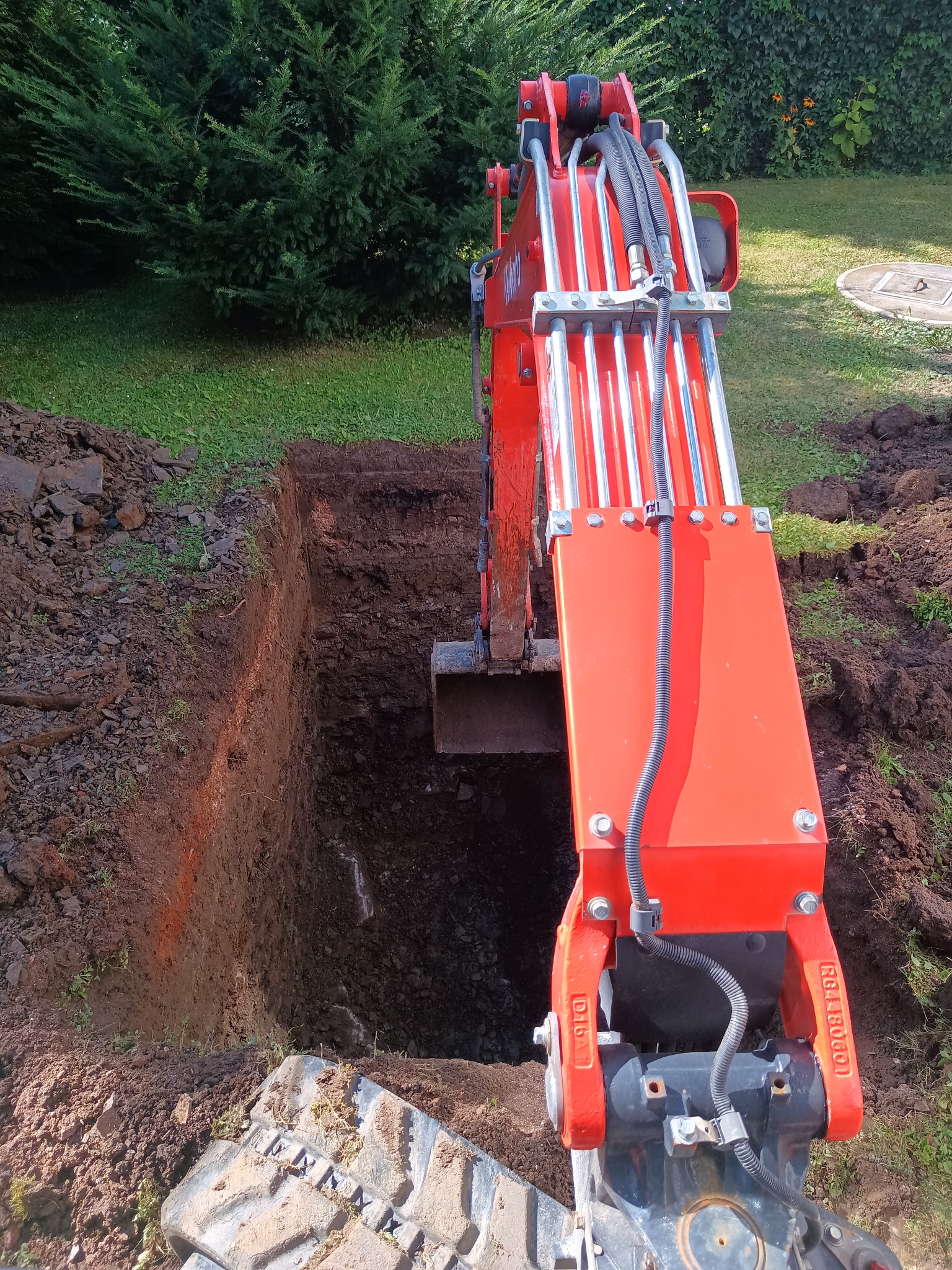 Czerwona koparka w trakcie prac ziemnych, głęboki wykop w Bielowicku, widoczne ślady świeżo wykopanej ziemi i fragment opony koparki.