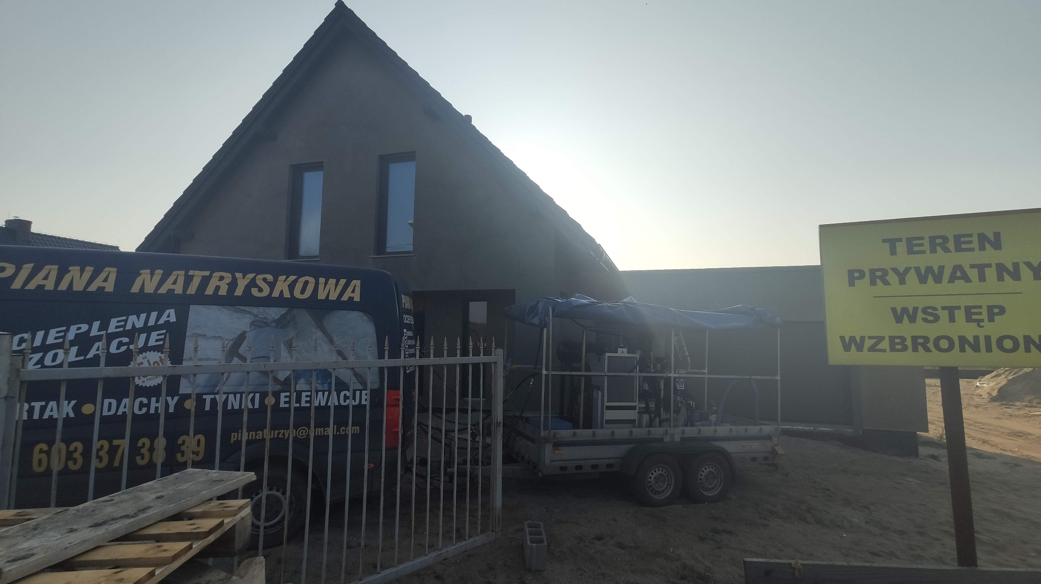 Ekipa ociepleniowa z wozem i busem na tle domu w trakcie budowy, widoczny napis na busie: Piana Natryskowa, teren prywatny.