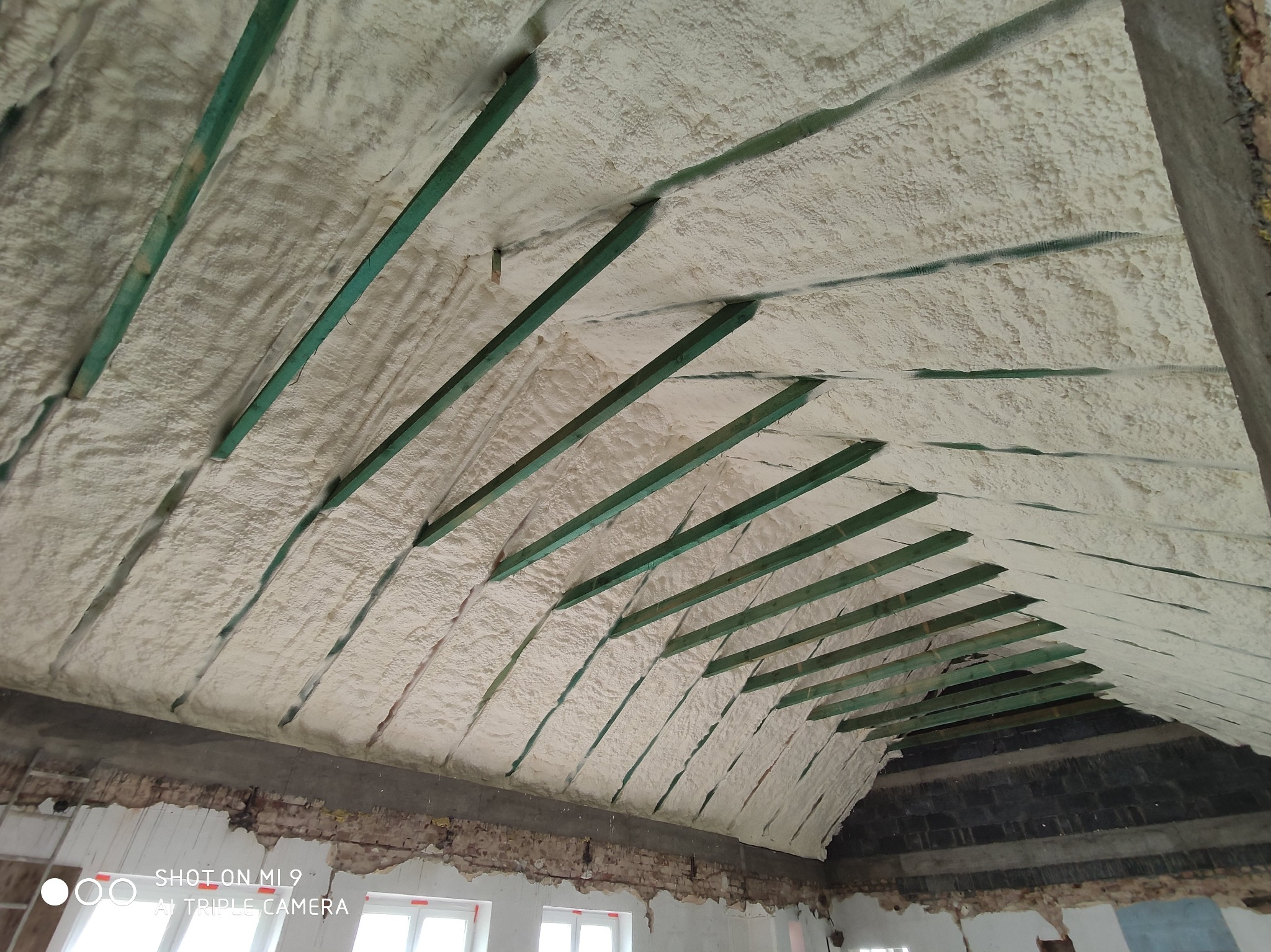 Poddasze z widocznymi krokwiami wypełnione białą pianą izolacyjną, widok z dołu, ściany w trakcie remontu.