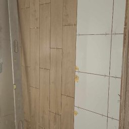 BAS - bełchcompany - W trakcie układania płytek imitujących drewno na ścianie, obok białe płytki z krzyżykami dystansowymi, poziomica oparta o ścianę.