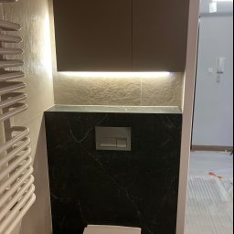 Bogdan Andriushkin - Nowoczesna łazienka po remoncie: podwieszana toaleta z czarnym marmurem, szafka z oświetleniem LED i grzejnik drabinkowy. Widok na wykończone wnętrze.