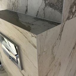 Bogdan Andriushkin - Wykończona toaleta w łazience z marmurowymi płytkami i chromowanym przyciskiem spłukiwania. Minimalistyczny design, eleganckie wykończenie.