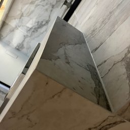 Bogdan Andriushkin - Wykończona ściana i fragment zabudowy w łazience, imitacja marmuru, szare i białe odcienie, nowoczesny design, widok pod kątem.