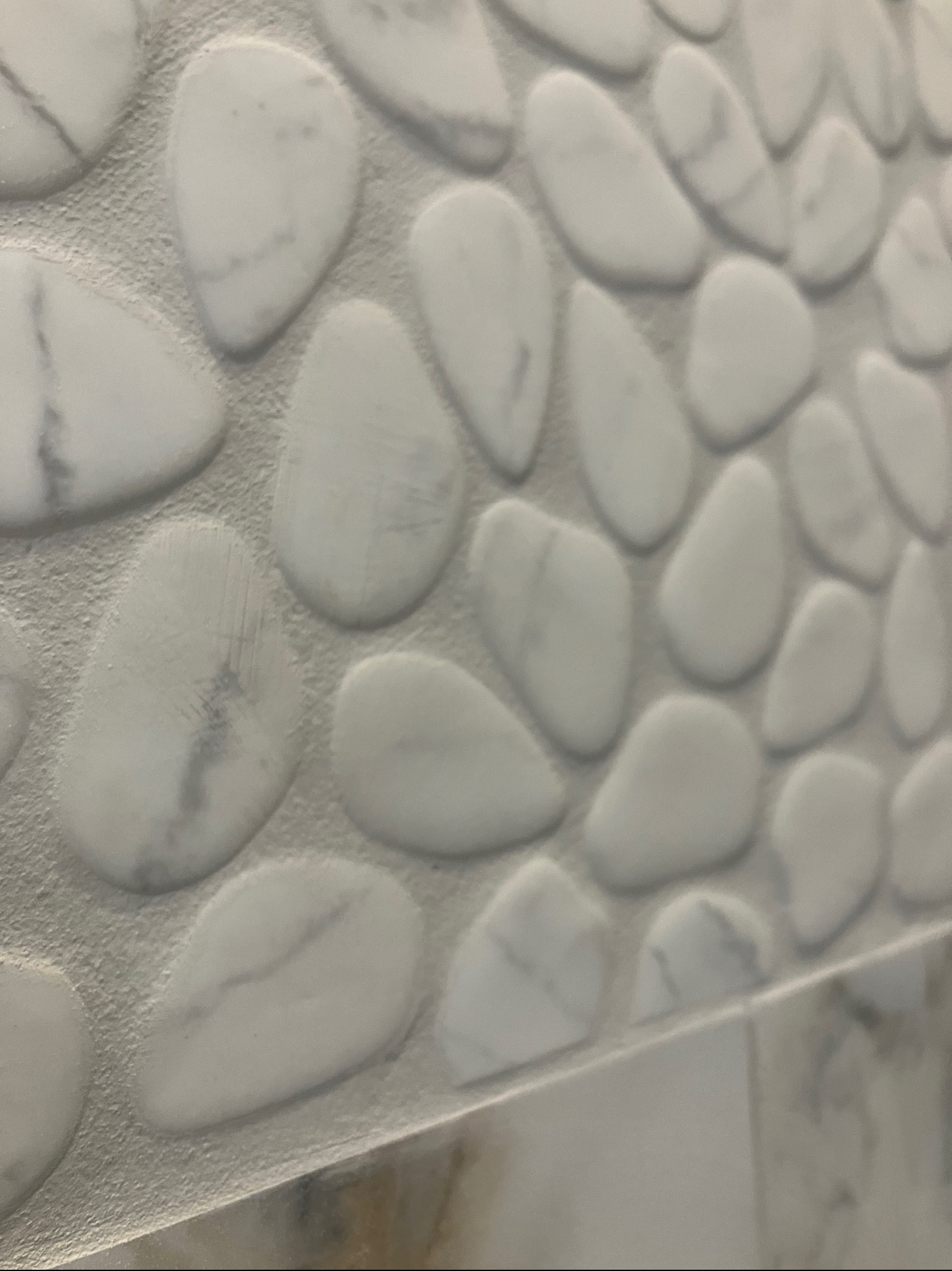 Biała mozaika imitująca kamienie na ścianie, z widocznymi fugami i delikatnym wzorem marmuru na poszczególnych elementach. Wykończenie łazienki w zbliżeniu.