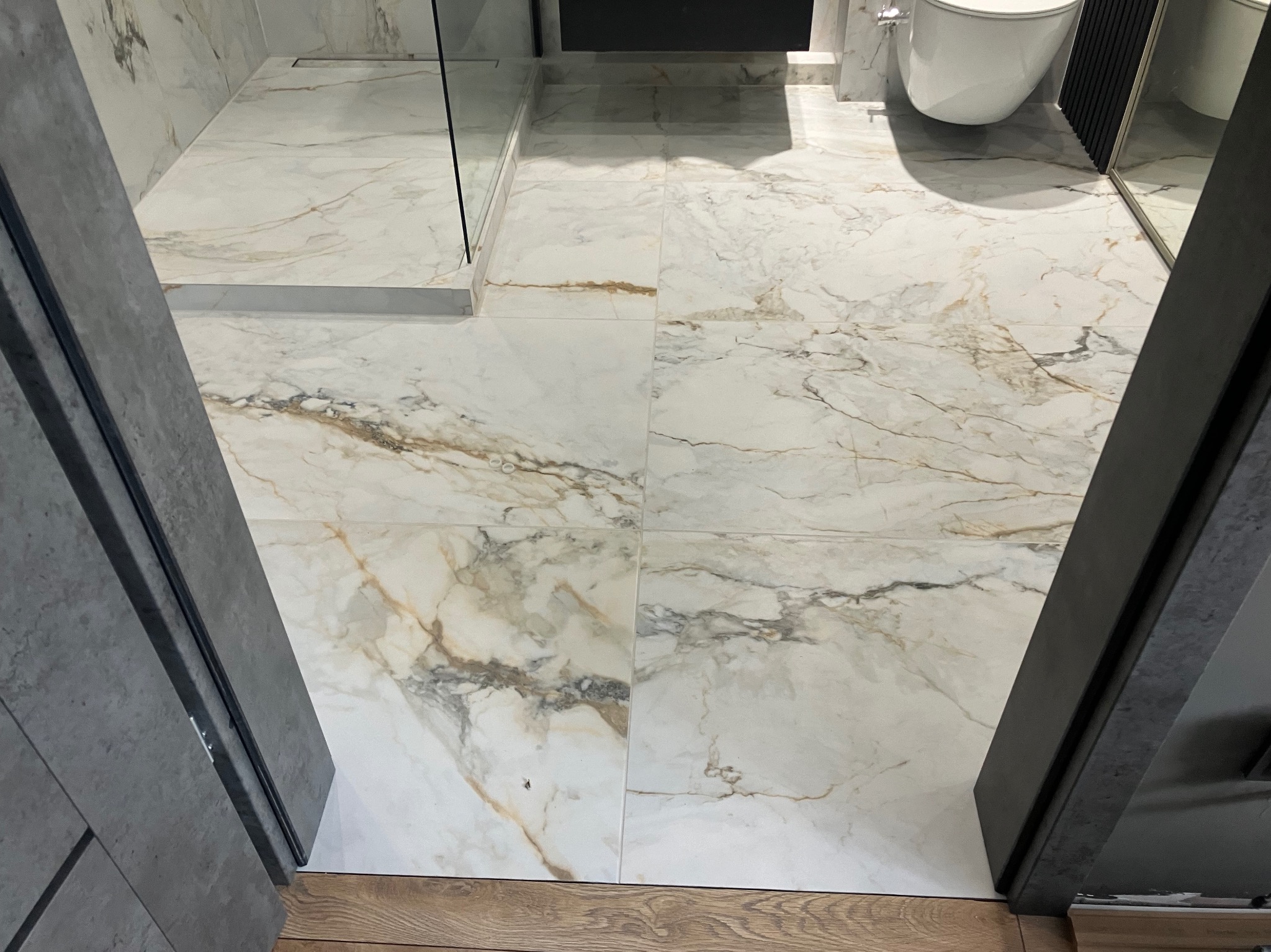 Wykończona łazienka z marmurową podłogą i kabiną prysznicową. Widok z góry, z otwartymi drzwiami. Uwagę przykuwa wzór marmuru i nowoczesny design.