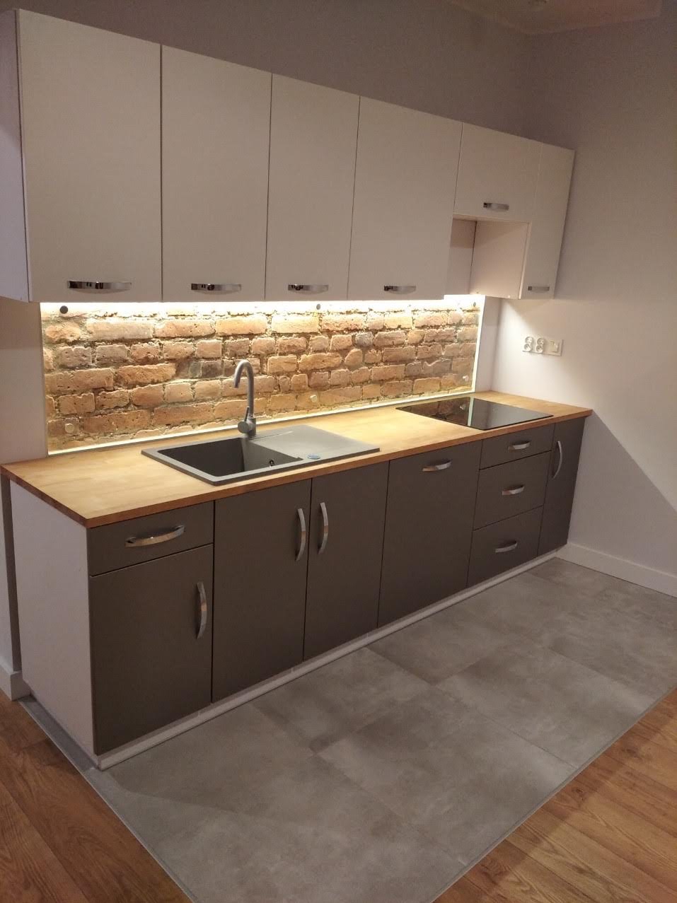 Nowoczesna kuchnia z białymi szafkami górnymi i brązowymi dolnymi. Ceglana ściana nad blatem podświetlona LED. Umywalka ze stali nierdzewnej. Minimalistyczny design.