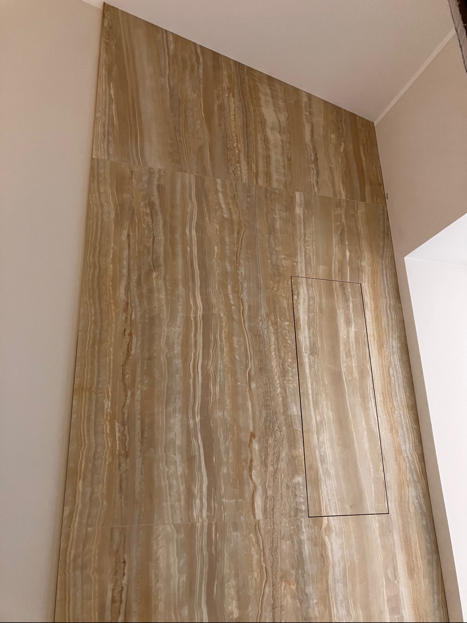 Ściana wykończona płytami imitującymi trawertyn, z ukrytymi drzwiczkami rewizyjnymi. Ukośne ułożenie płyt tworzy unikalny efekt wizualny.