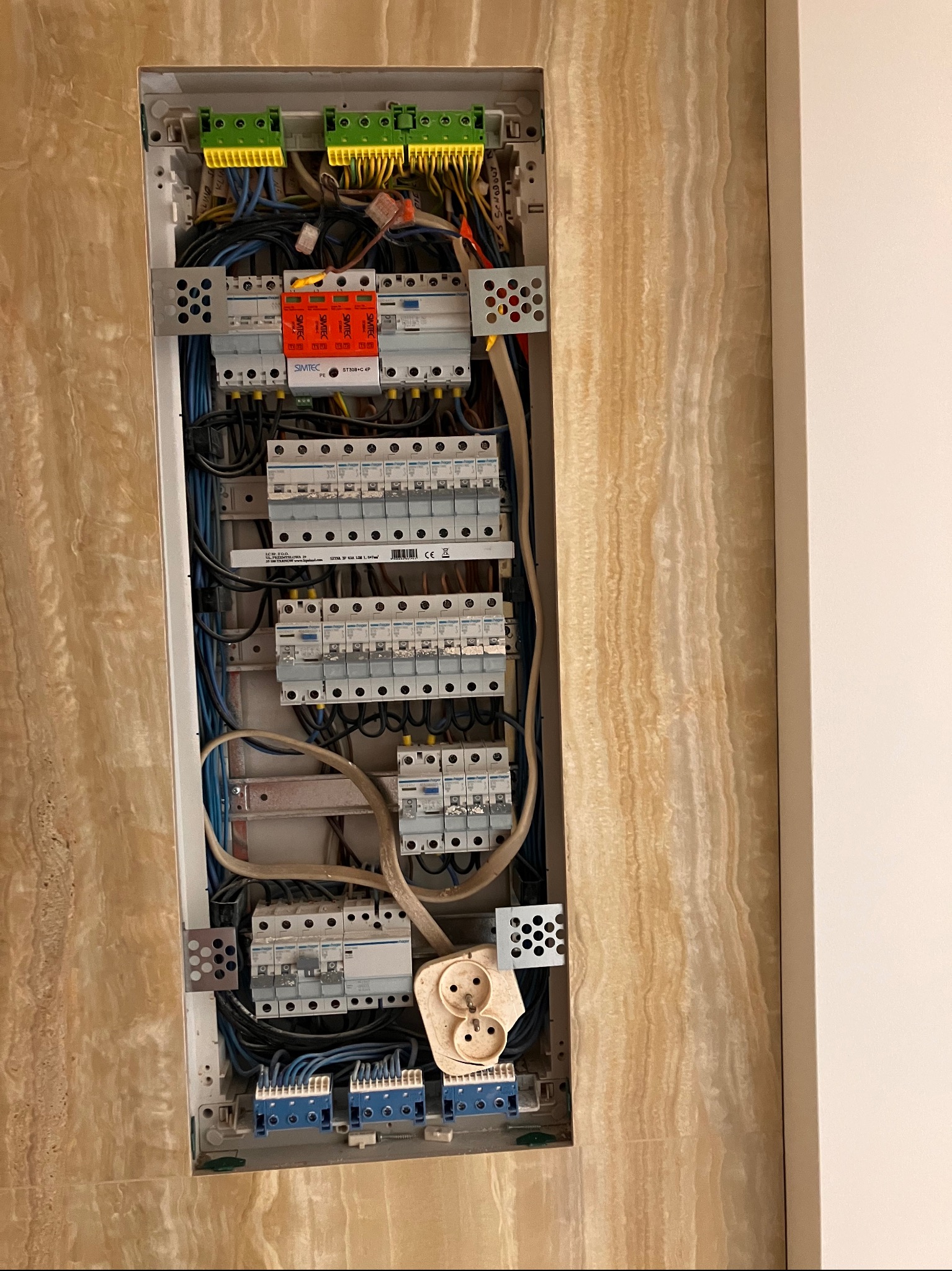 Rozdzielnia elektryczna wnękowa z bezpiecznikami, okablowaniem i gniazdem, zamontowana na ścianie z beżowego marmuru. Widok z góry, detale instalacji.