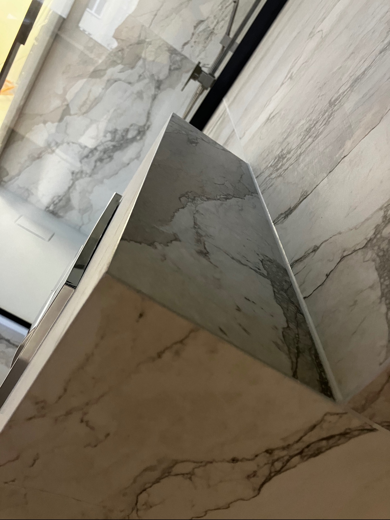 Wykończona ściana i fragment zabudowy w łazience, imitacja marmuru, szare i białe odcienie, nowoczesny design, widok pod kątem.