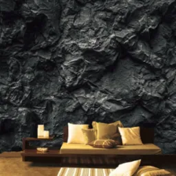 Ściana imitująca surowy kamień w ciemnej kolorystyce, stanowiąca tło dla minimalistycznego salonu z beżową sofą, poduszkami i dywanem w paski.