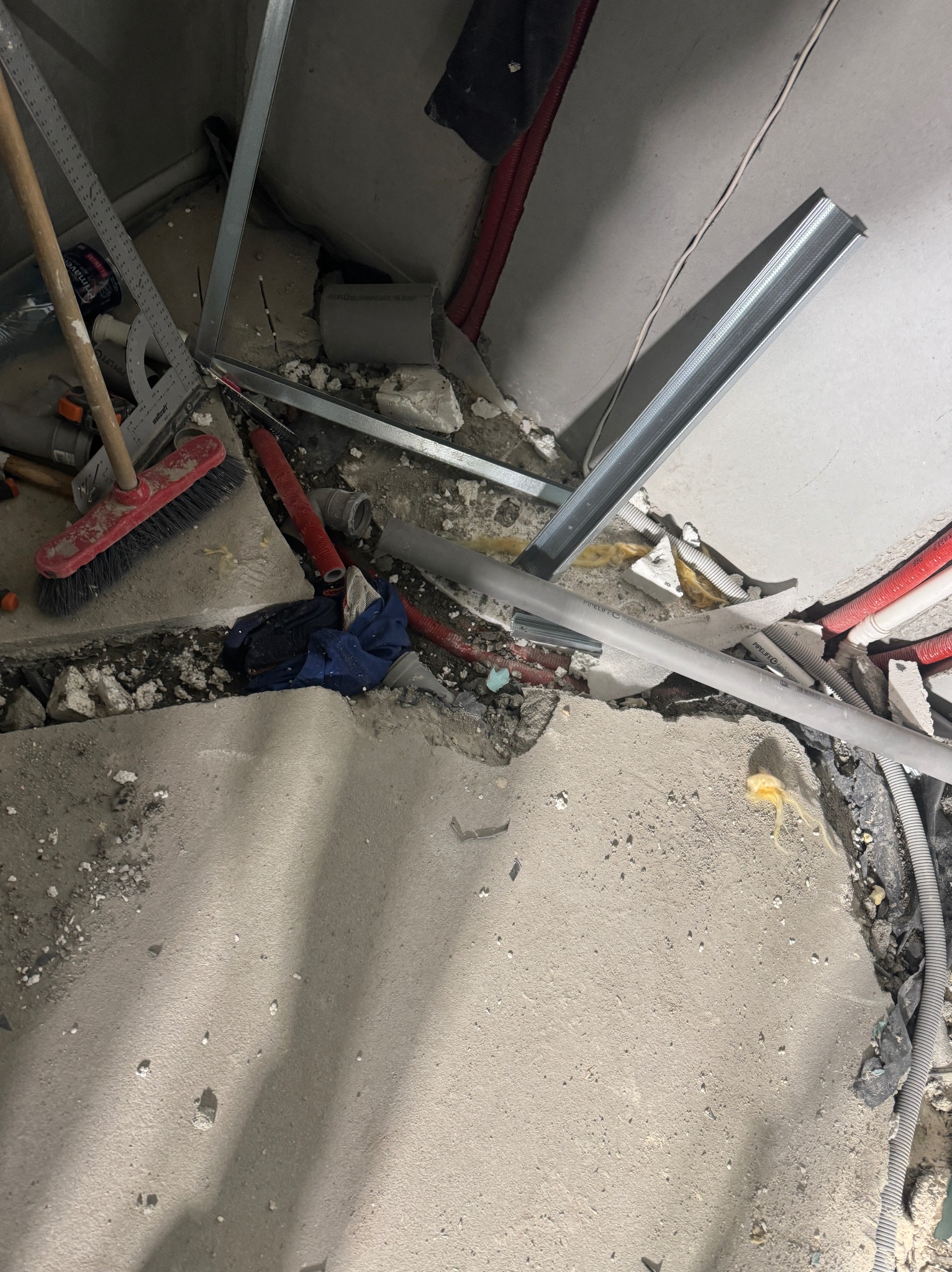 Fragment podłogi w trakcie remontu z widocznymi elementami konstrukcji metalowej, rurami, przewodami, narzędziami i gruzem.