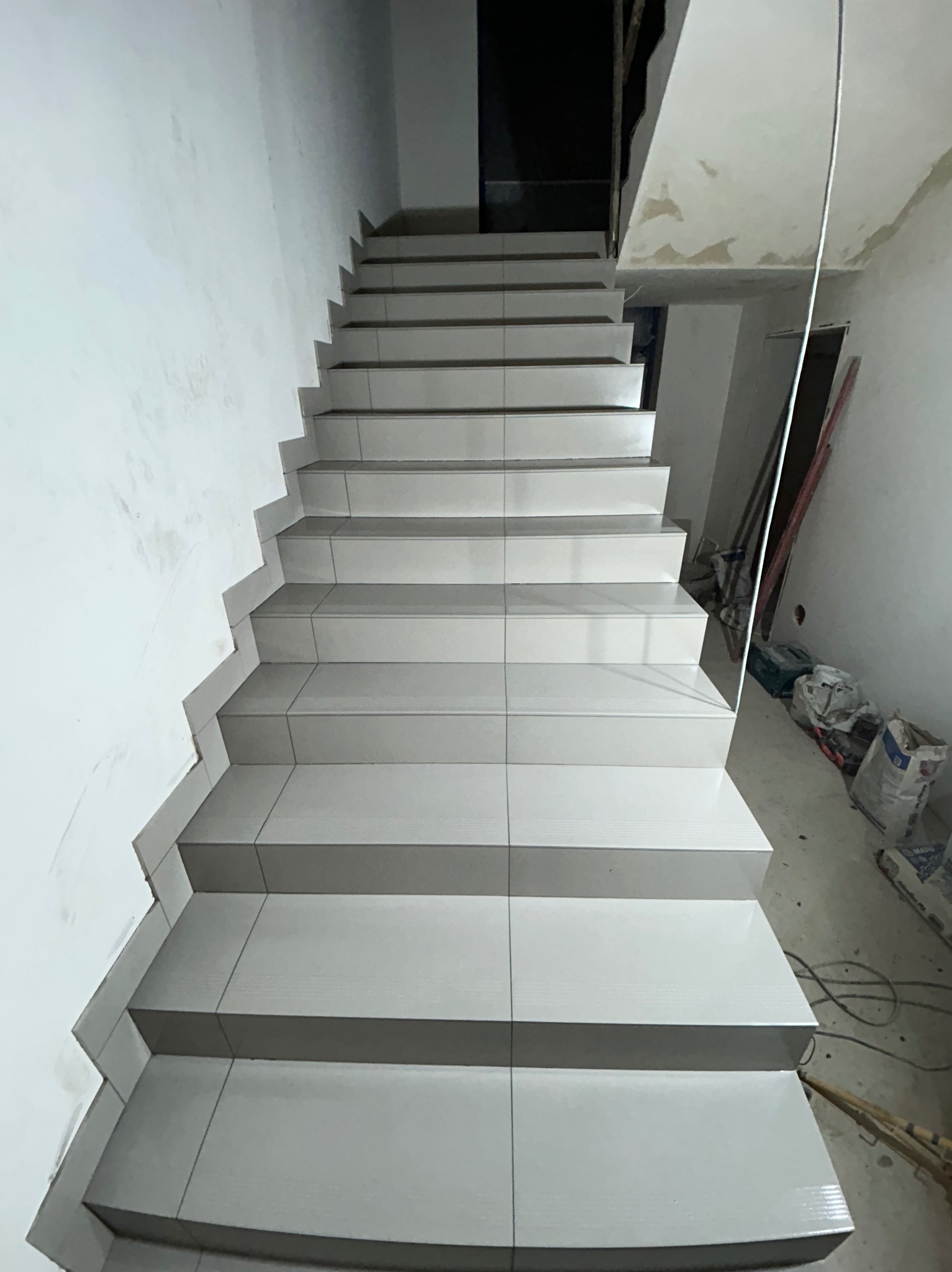 Wykończone schody wewnętrzne z szarych płytek ceramicznych, widok z dołu, w tle surowe ściany w trakcie remontu.