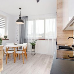 Quality Apartments - Jasna kuchnia z okrągłym stołem, białymi krzesłami i czarnym zlewem na tle wzorzystych płytek.