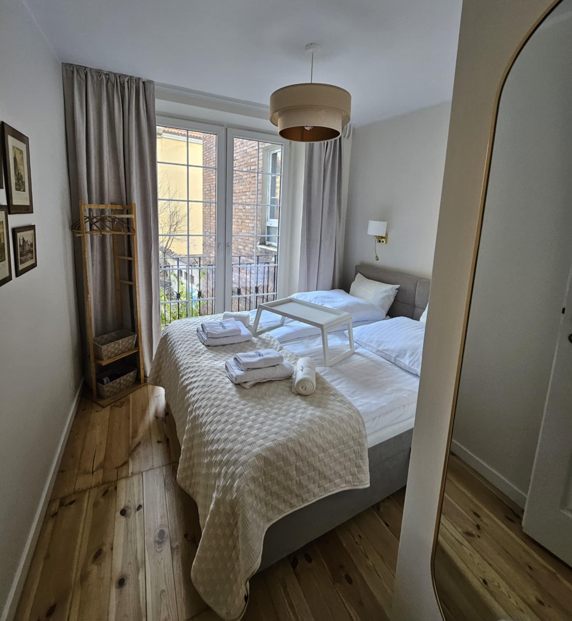 Jasna sypialnia z dwoma łóżkami, balkonem i drewnianą podłogą, widoczne ręczniki i stolik śniadaniowy.