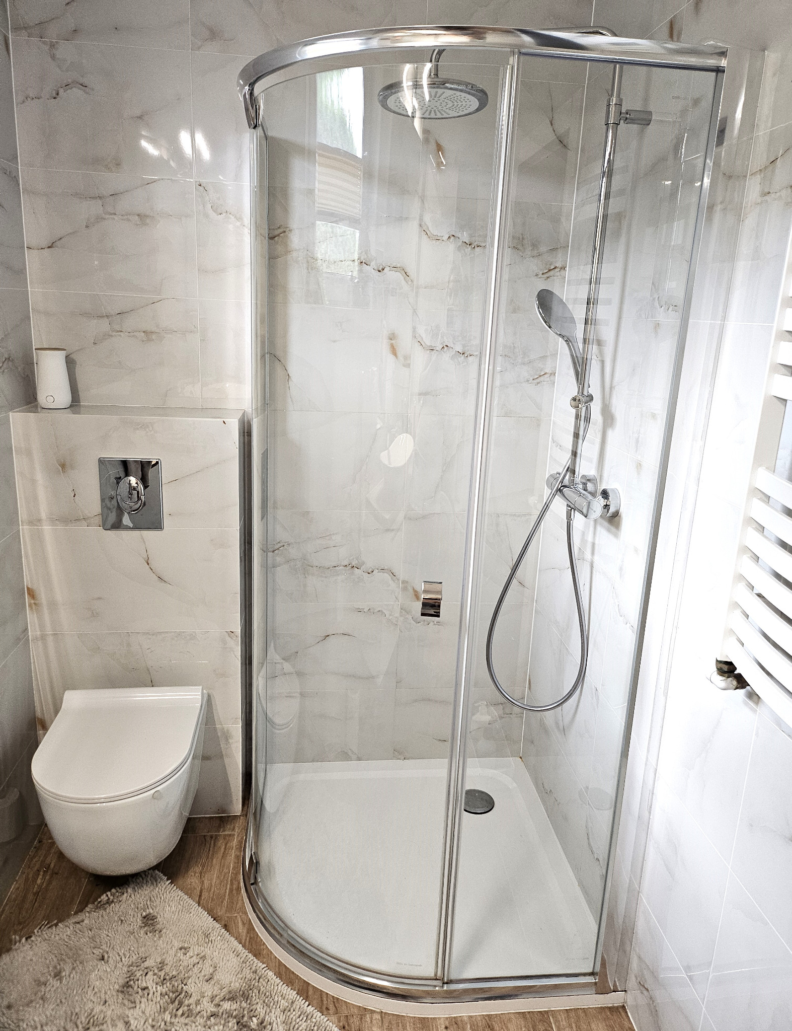 Nowoczesna łazienka z kabiną prysznicową typu walk-in, wiszącą toaletą i marmurowymi płytkami ściennymi z delikatnym żyłkowaniem.