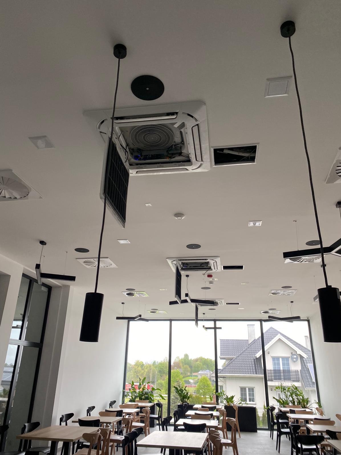 Kasetonowa jednostka klimatyzacyjna w suficie podwieszanym restauracji, z otwartym panelem dostępowym, widoczne wnętrze urządzenia i elementy instalacji.