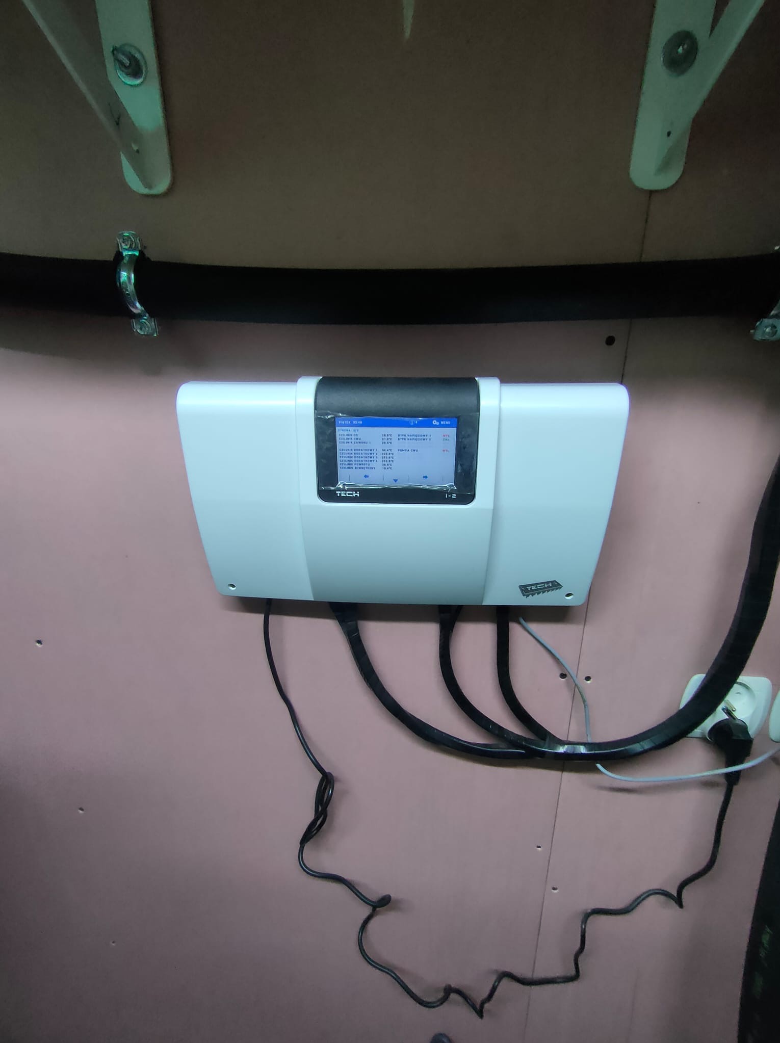 Biały regulator solarny TECH zamontowany na różowej ścianie, widoczne czarne kable i gniazdko elektryczne.