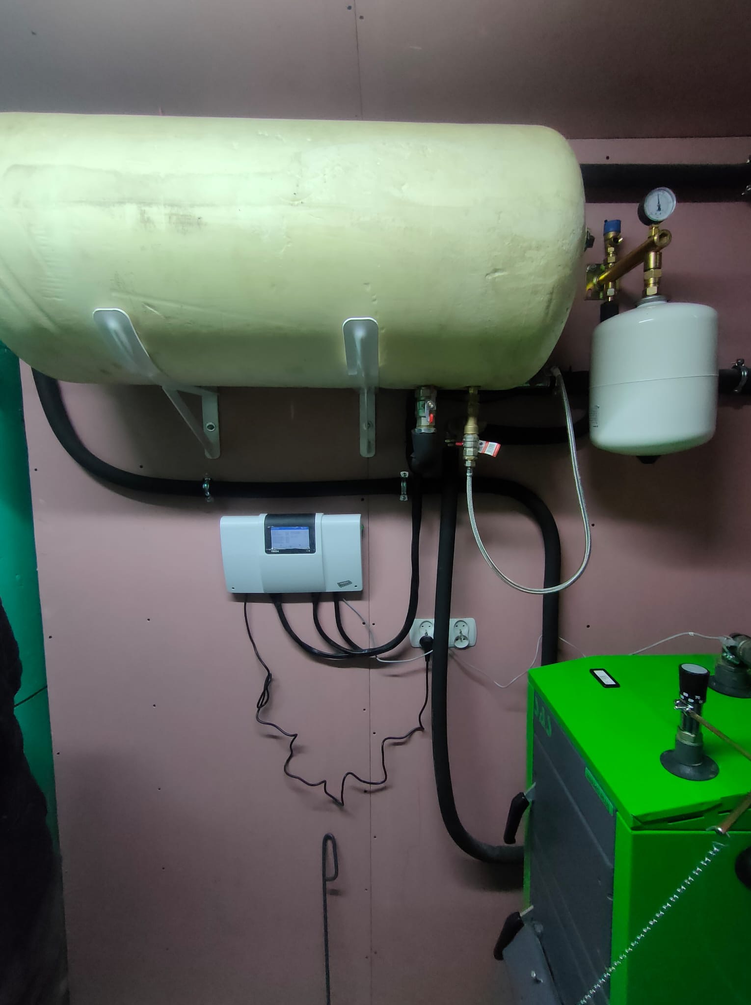 Elementy instalacji grzewczej: zbiornik akumulacyjny, naczynie wzbiorcze, sterownik i zielony piec, widoczne przewody i rury.