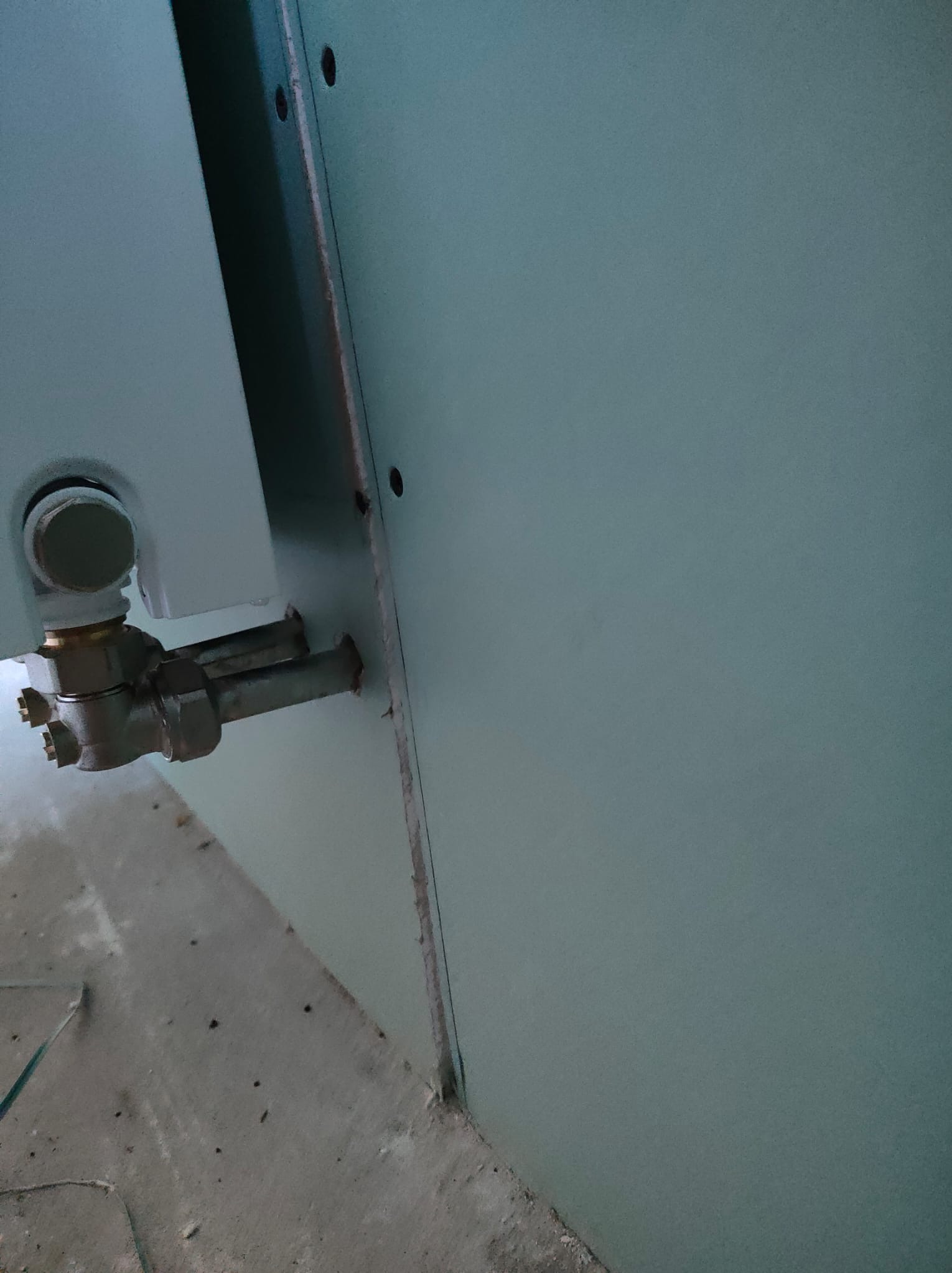 Szczegół montażu instalacji wewnątrz budynku: rury przytwierdzone do ściany z płyty kartonowo-gipsowej, widoczne elementy instalacji i fragment podłogi w stanie surowym.