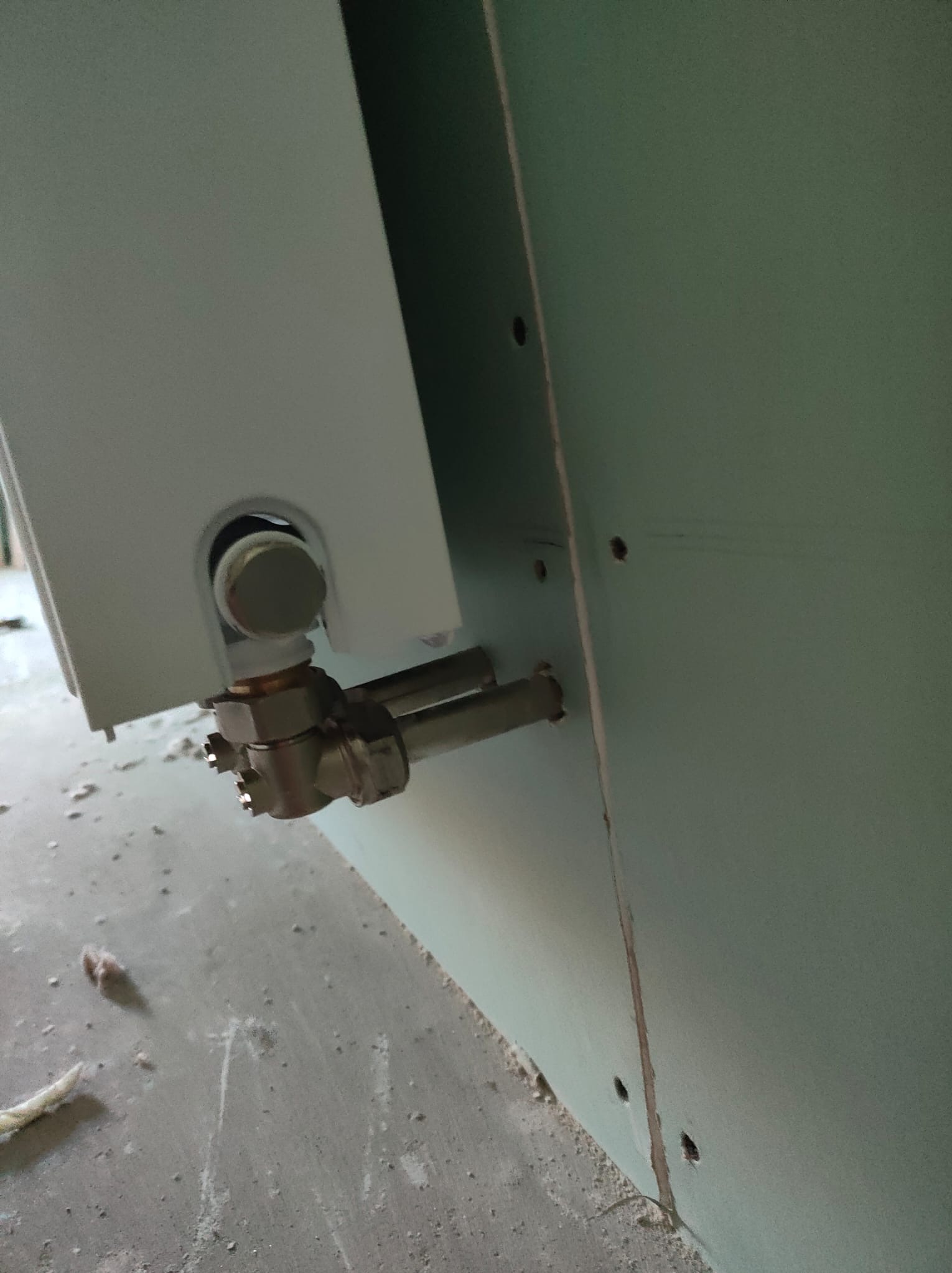 Montaż instalacji grzewczej: przyłącze rur do białego bojlera na tle surowej ściany z płyt kartonowo-gipsowych.