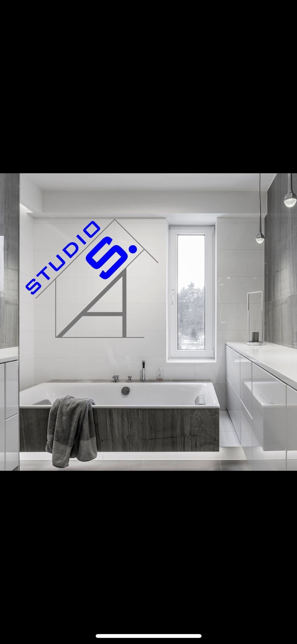 Nowoczesna łazienka z białą wanną obudowaną ciemnym drewnem, szara podłoga, białe płytki i szafki, okno z widokiem na zimowy krajobraz, designerskie oświetlenie, ręcznik na wannie oraz logo firmy...