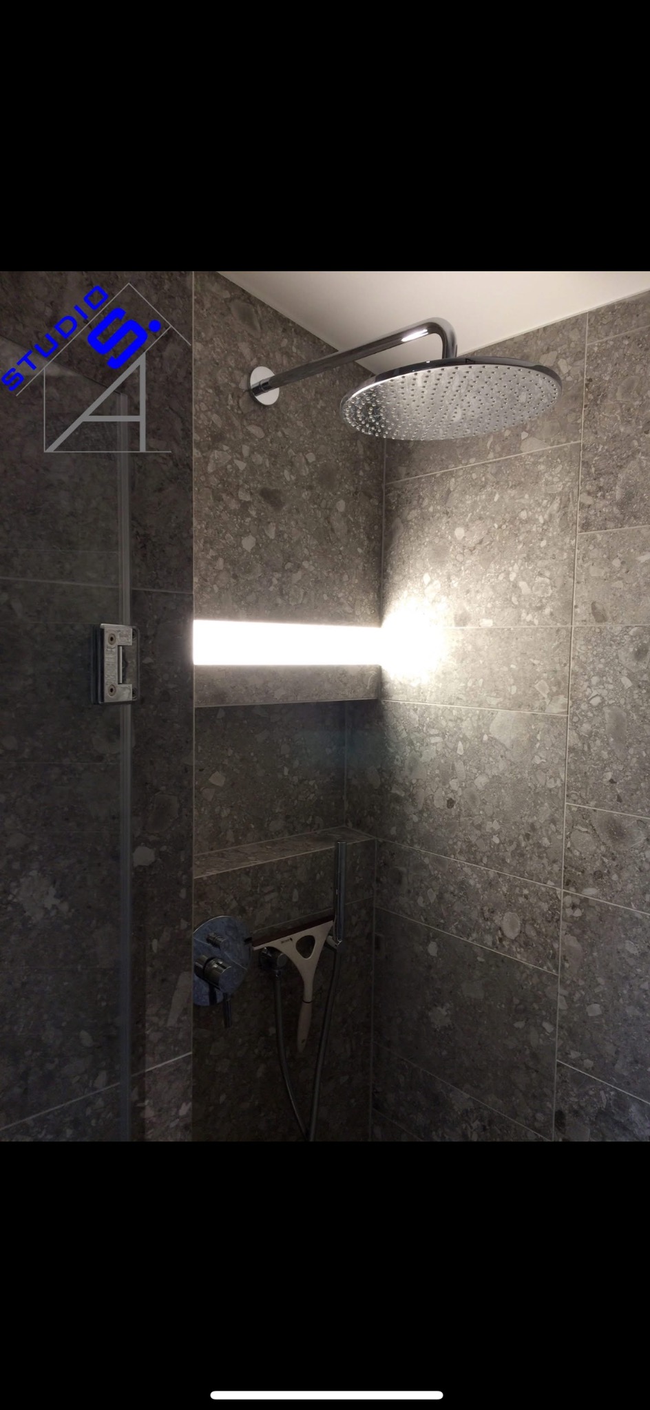 Nowoczesna kabina prysznicowa z deszczownicą, szarymi płytkami imitującymi kamień i wnęką z podświetleniem LED, widoczny uchwyt na ściągaczkę do szyb.