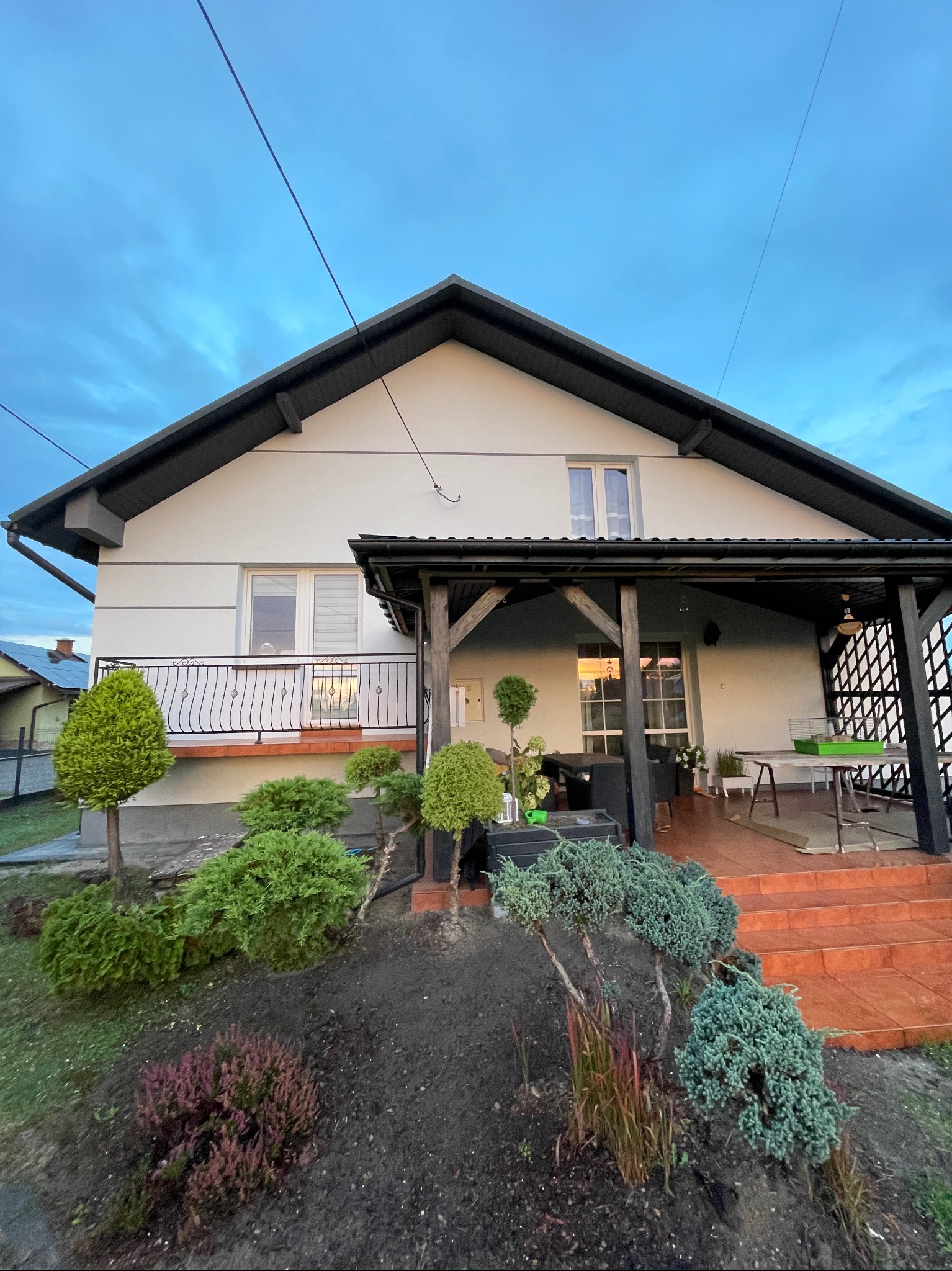 Front domu jednorodzinnego z werandą i zadbanym ogrodem z iglakami, widok na elewację i wejście do domu.