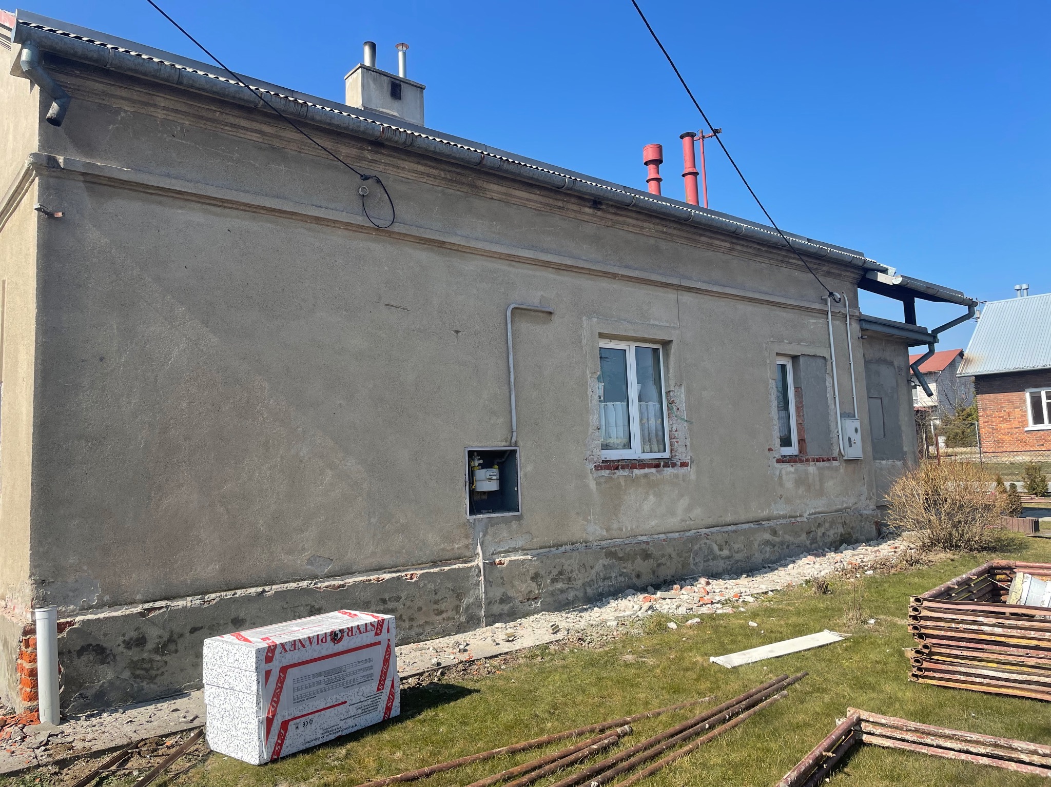 Styropian na trawie przed budynkiem z uszkodzoną elewacją, widoczne przygotowania do prac ociepleniowych.