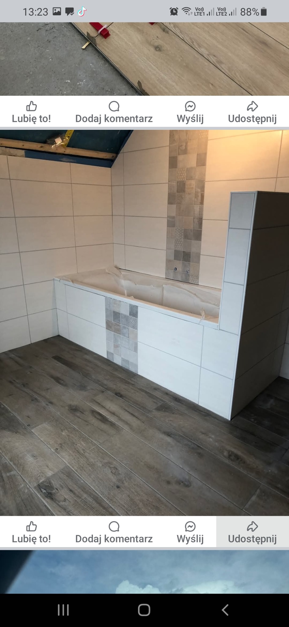 Wykończona łazienka z drewnopodobną podłogą, białą zabudową wanny z szarymi akcentami mozaiki i świeżo położonymi białymi płytkami na ścianach.