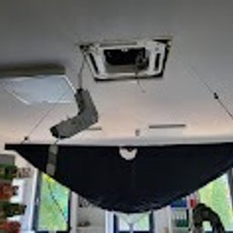 Montaż klimatyzacji kasetonowej w biurze: widoczny otwarty panel sufitowy, podwieszona osłona ochronna i narzędzia. Ujęcie z dołu, oświetlenie mieszane.