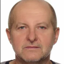 Portret mężczyzny z krótką, siwiejącą brodą na białym tle.