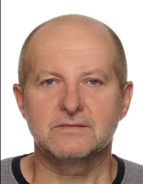 Portret mężczyzny z krótką, siwiejącą brodą na białym tle.