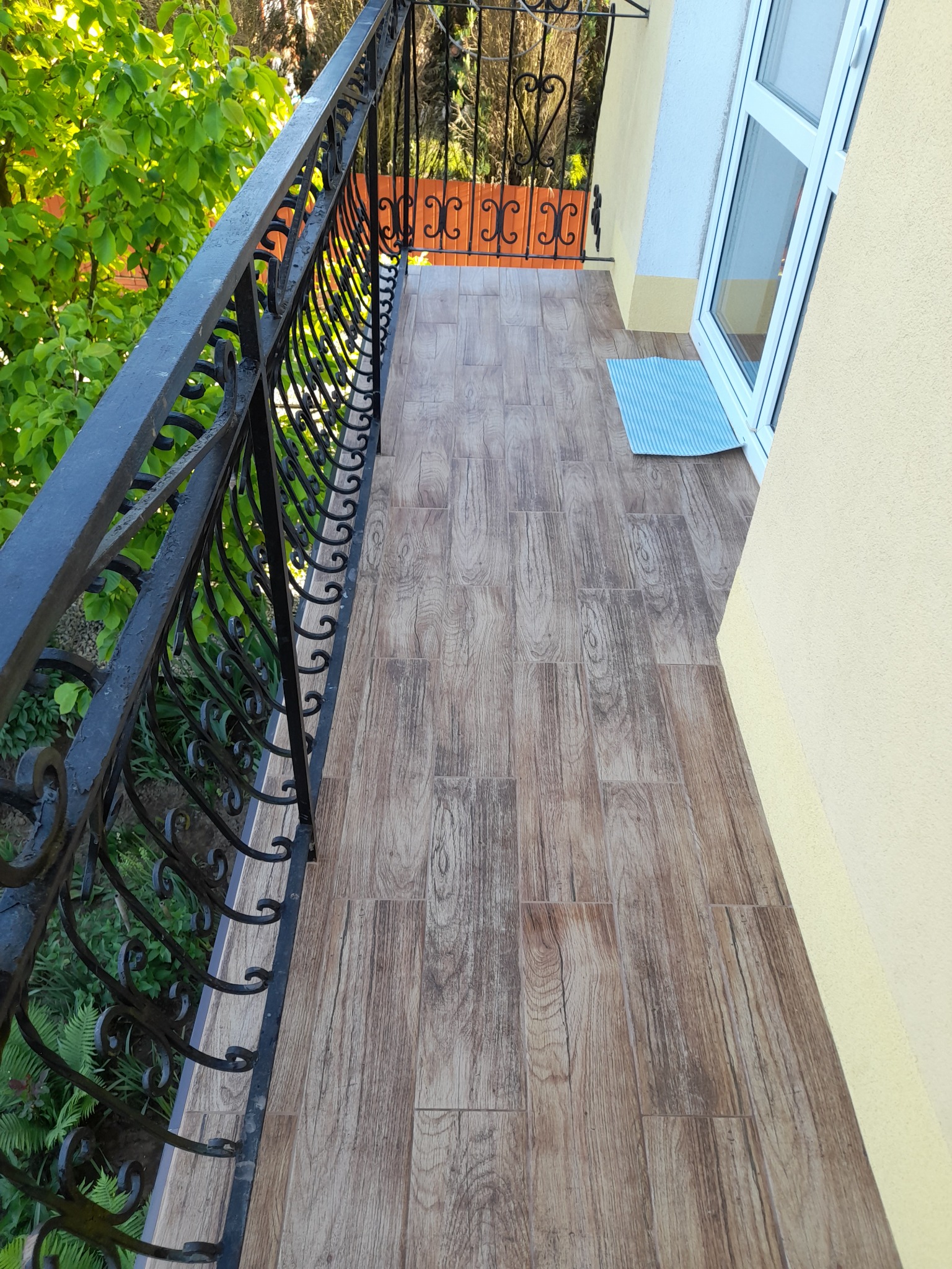 Balkon w Bachórzcu z nową podłogą imitującą drewno i ozdobną, czarną balustradą, widok z góry.