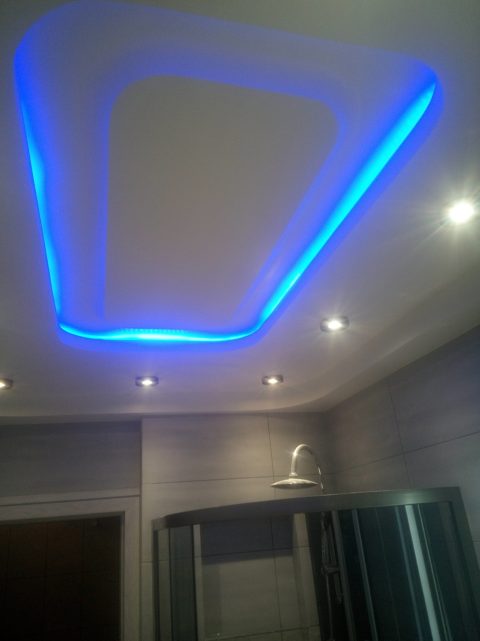 Nowoczesna łazienka z podświetlanym sufitem w geometrycznym kształcie, minimalistyczny design z szarymi płytkami i kabiną prysznicową.