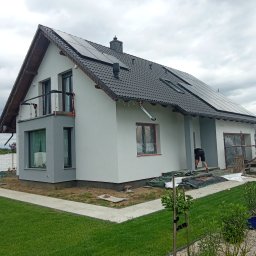G.M Complex -Profi - Nowoczesny dom jednorodzinny z panelami słonecznymi na dachu, z szarym wykończeniem elewacji i pracami wykończeniowymi w toku, widok z ogrodu.